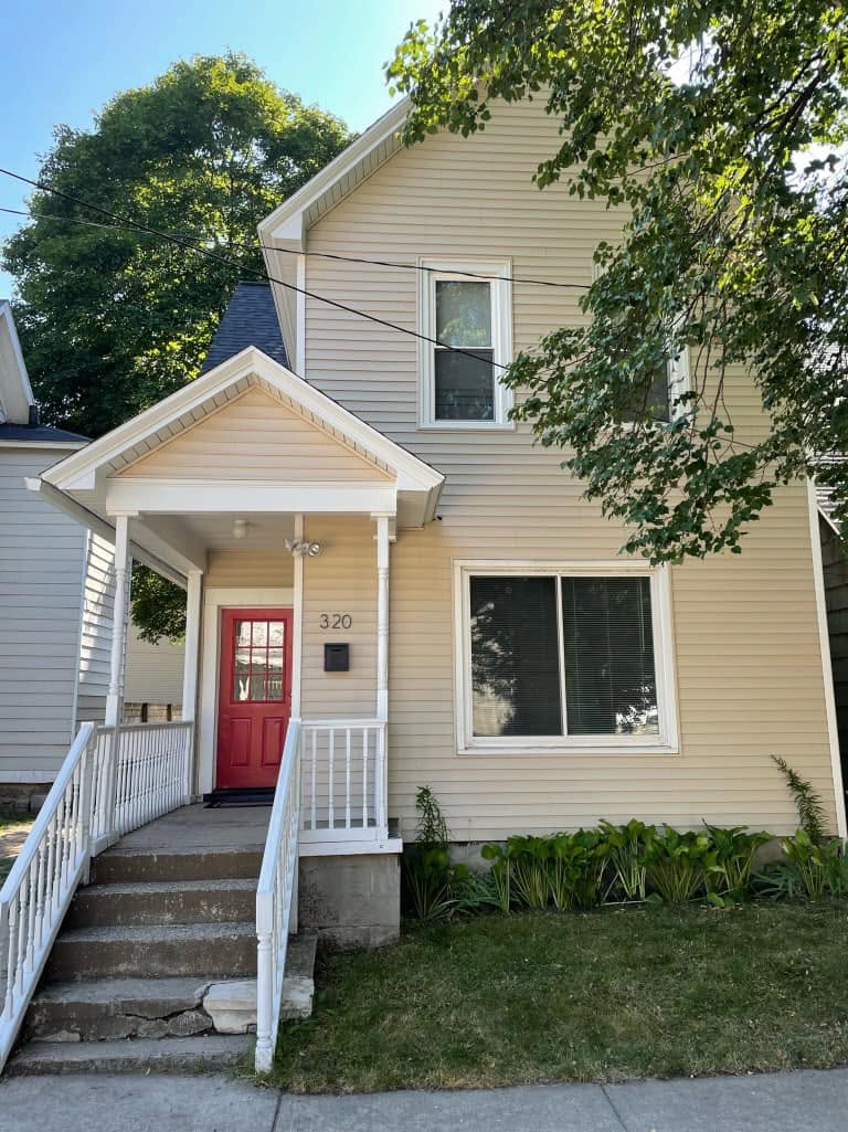 Front entrance of a two-story yellow house with a red door and covered porch